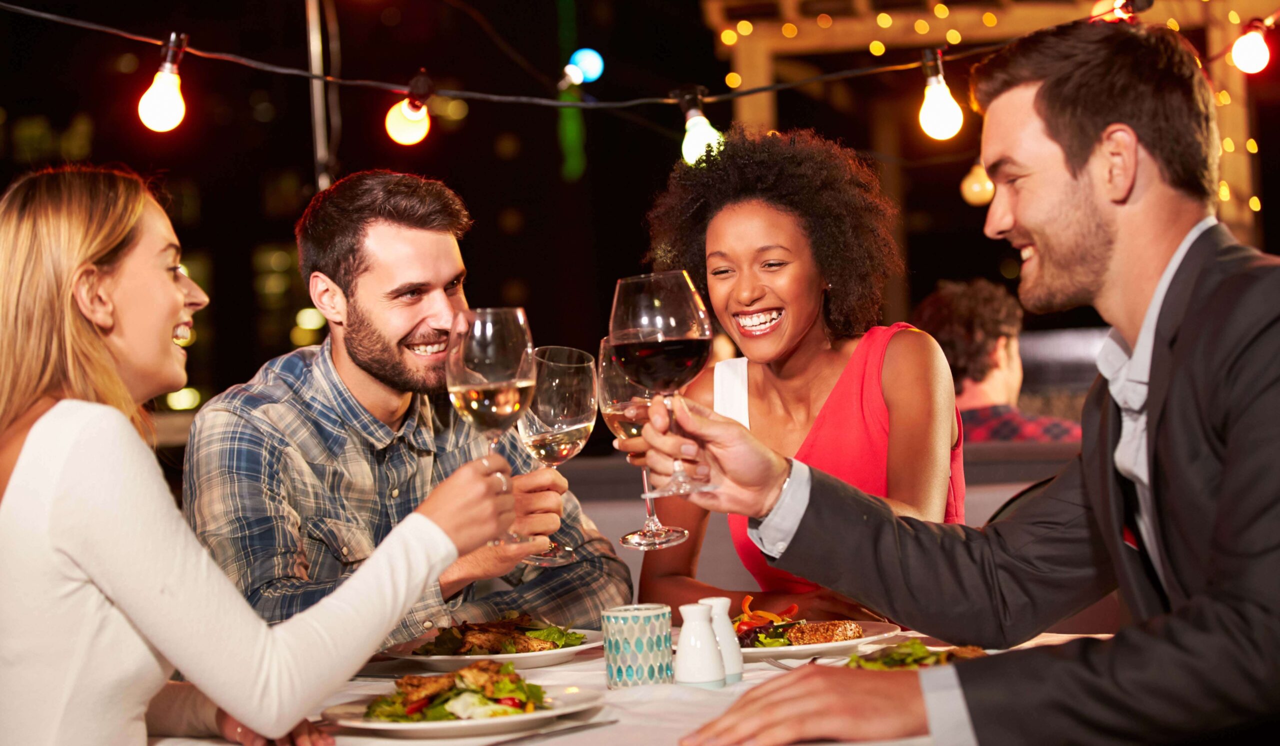 Group of friends enjoying dinner and wine at an outdoor restaurant in Midtown Manhattan at night