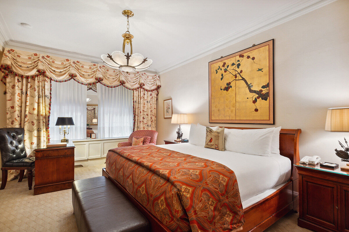 Elegant hotel room with a king bed featuring a red paisley coverlet, floral drapes, a large framed Japanese-style botanical artwork, and classic wood furniture.