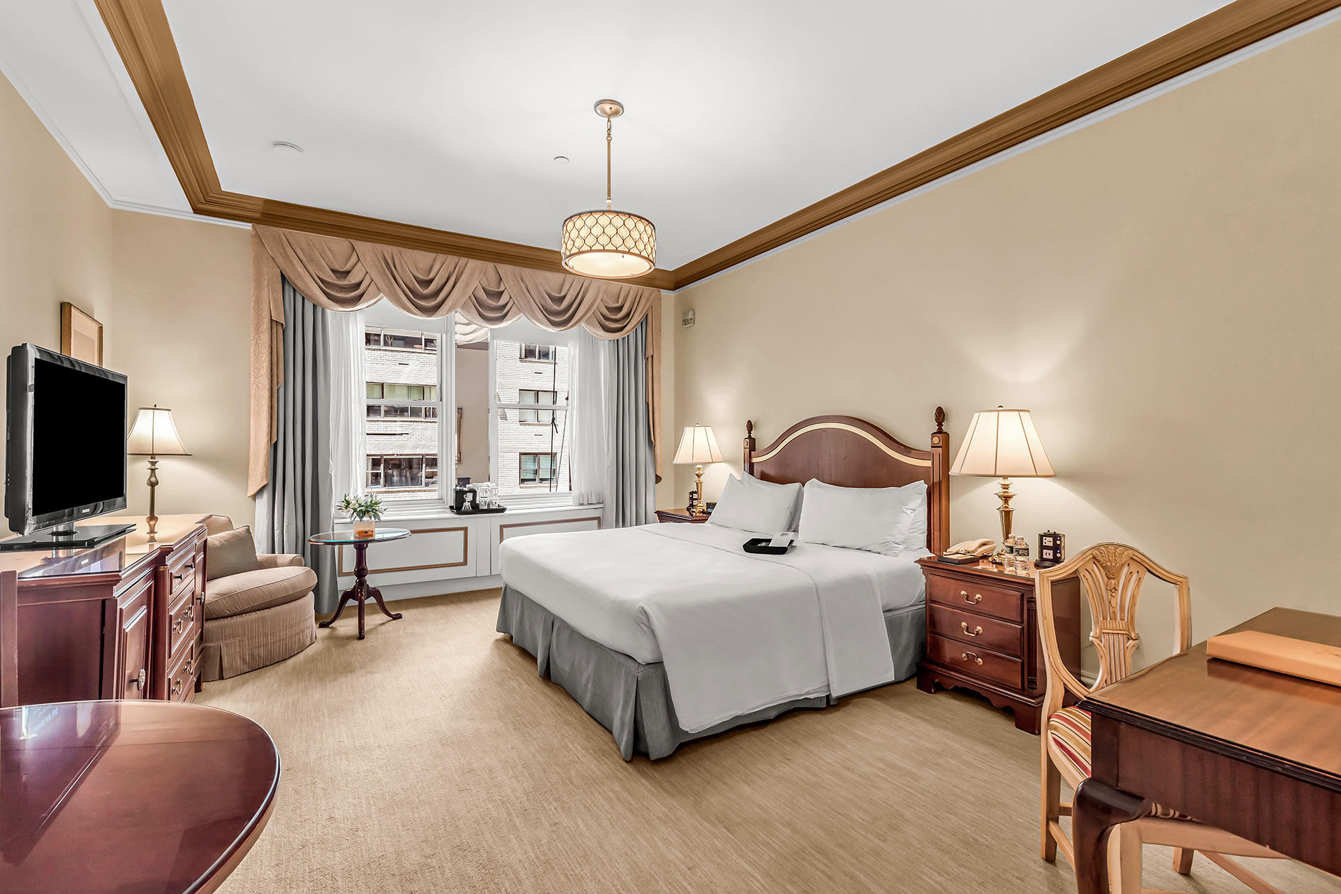 Spacious hotel room with classic decor, featuring a king bed, traditional wood furnishings, soft neutral tones, and a large window overlooking Midtown Manhattan.