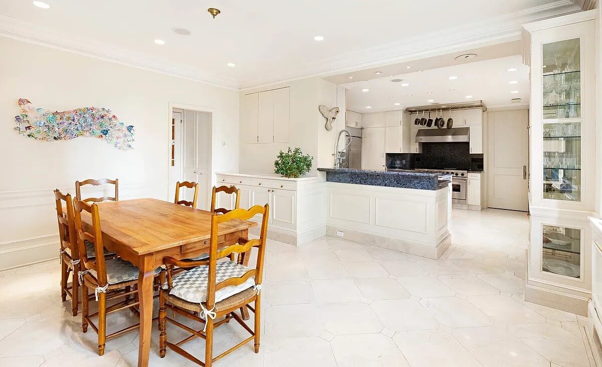 A bright and spacious dining area with a wooden table and chairs, leading into a modern kitchen with stainless steel appliances at The Sherry-Netherland.