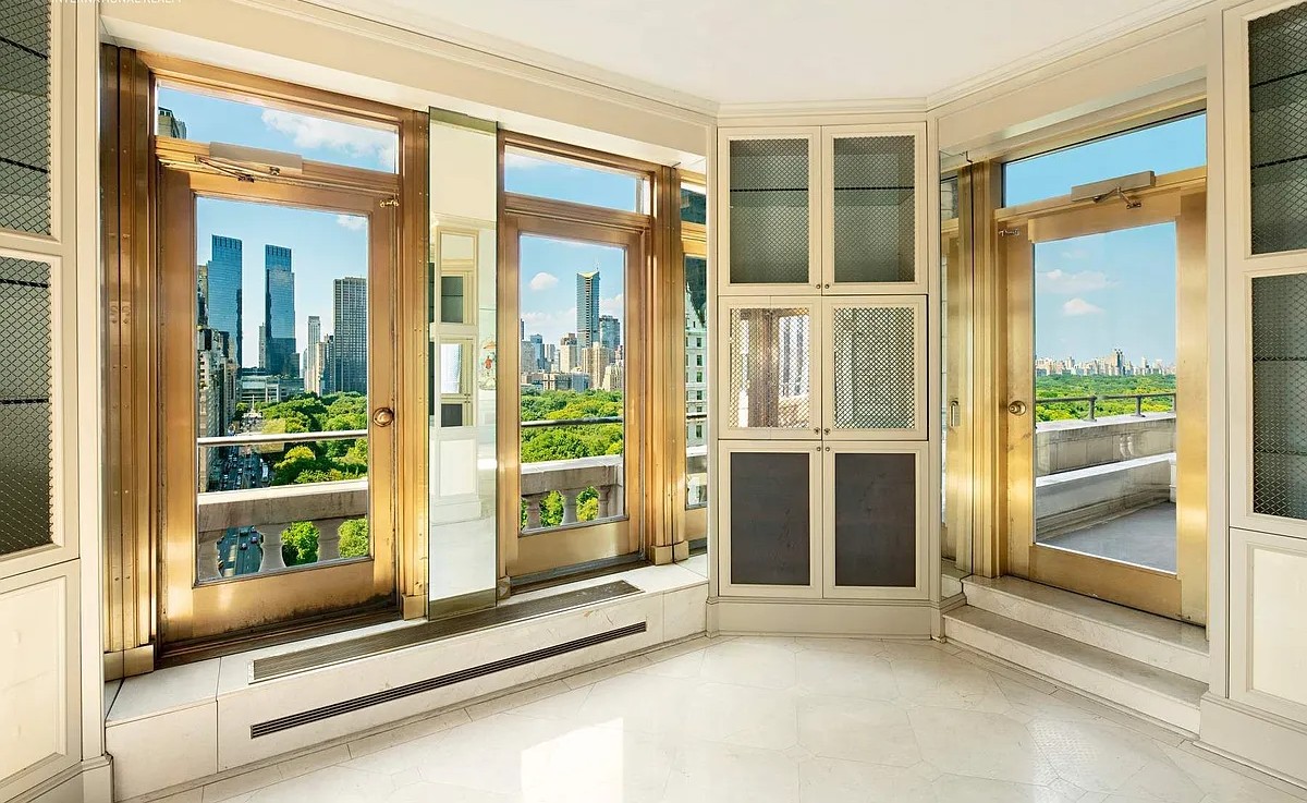 A sun-drenched room at The Sherry-Netherland with multiple sets of French doors framed in gold, opening to balconies with views of Central Park and the surrounding cityscape.