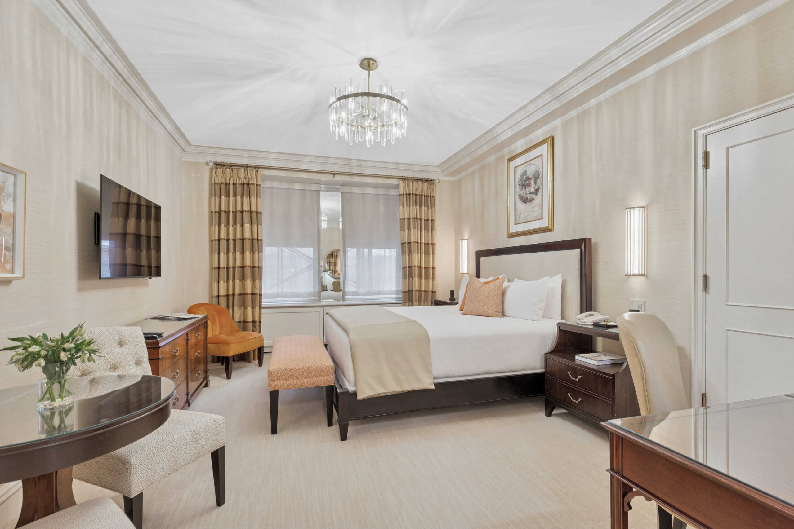 Elegant guest room featuring a king bed with cream linens, crystal chandelier, striped curtains, writing desk, upholstered seating, and classic wood furnishings.