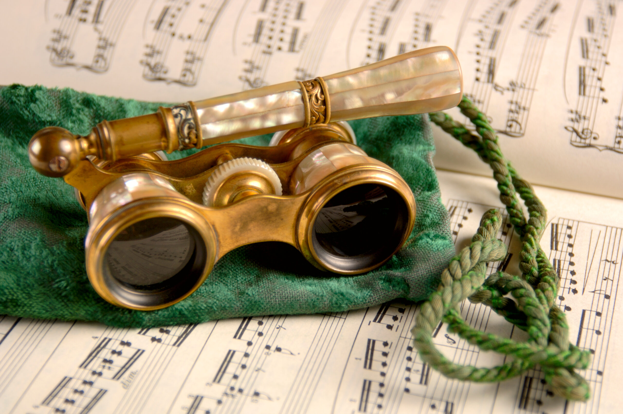 Vintage opera glasses with mother-of-pearl inlay resting on sheet music and a green velvet pouch