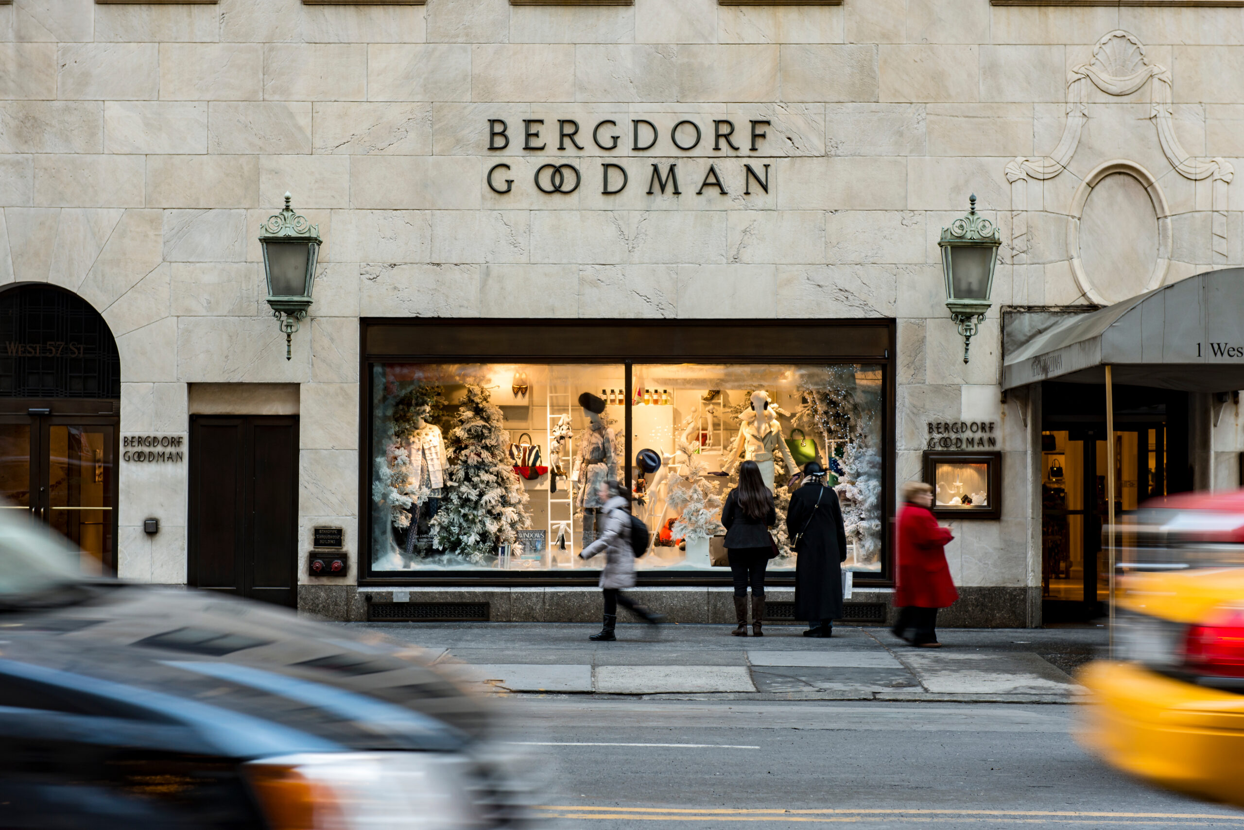 Shoppers admiring the holiday window display at Bergdorf Goodman on Fifth Avenue in New York City, with taxis and traffic passing by