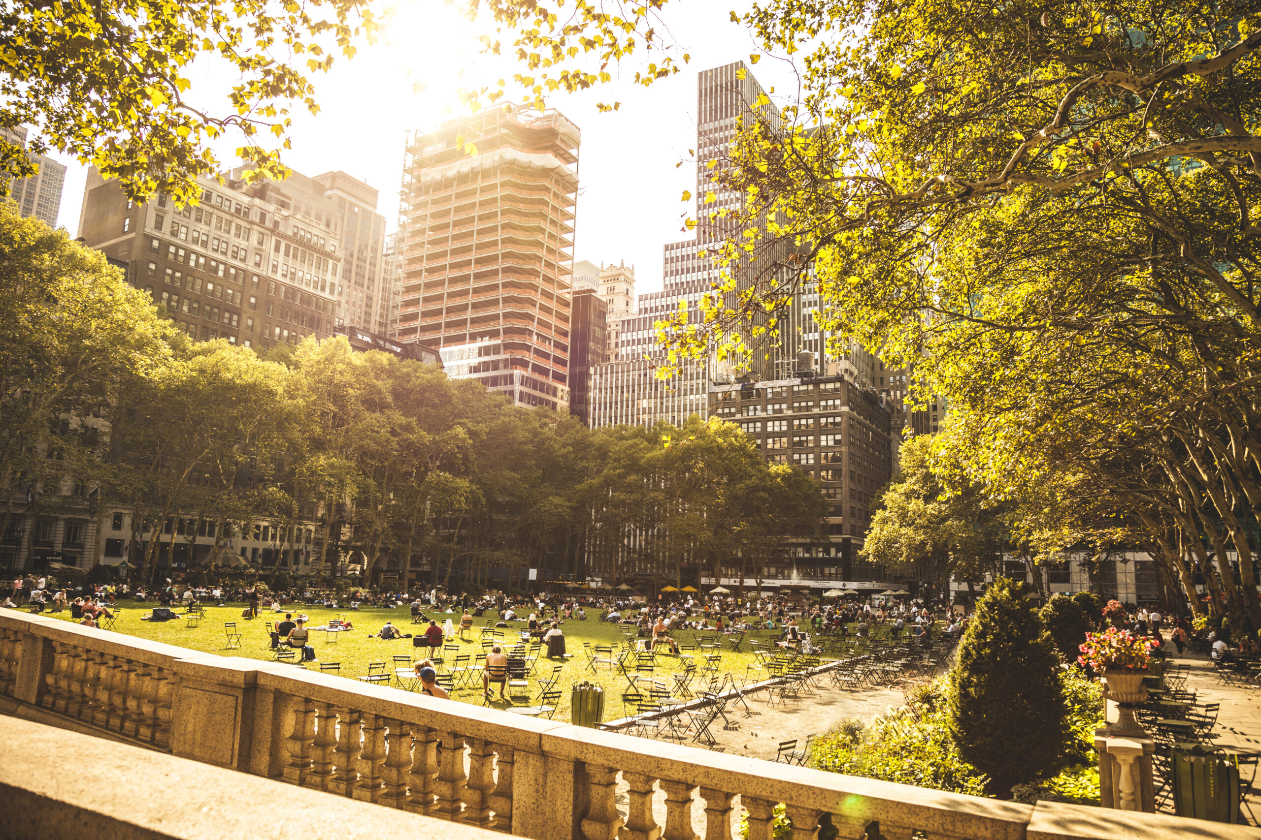 People relaxing in Bryant Park on a sunny day in New York City, surrounded by trees and skyscrapers