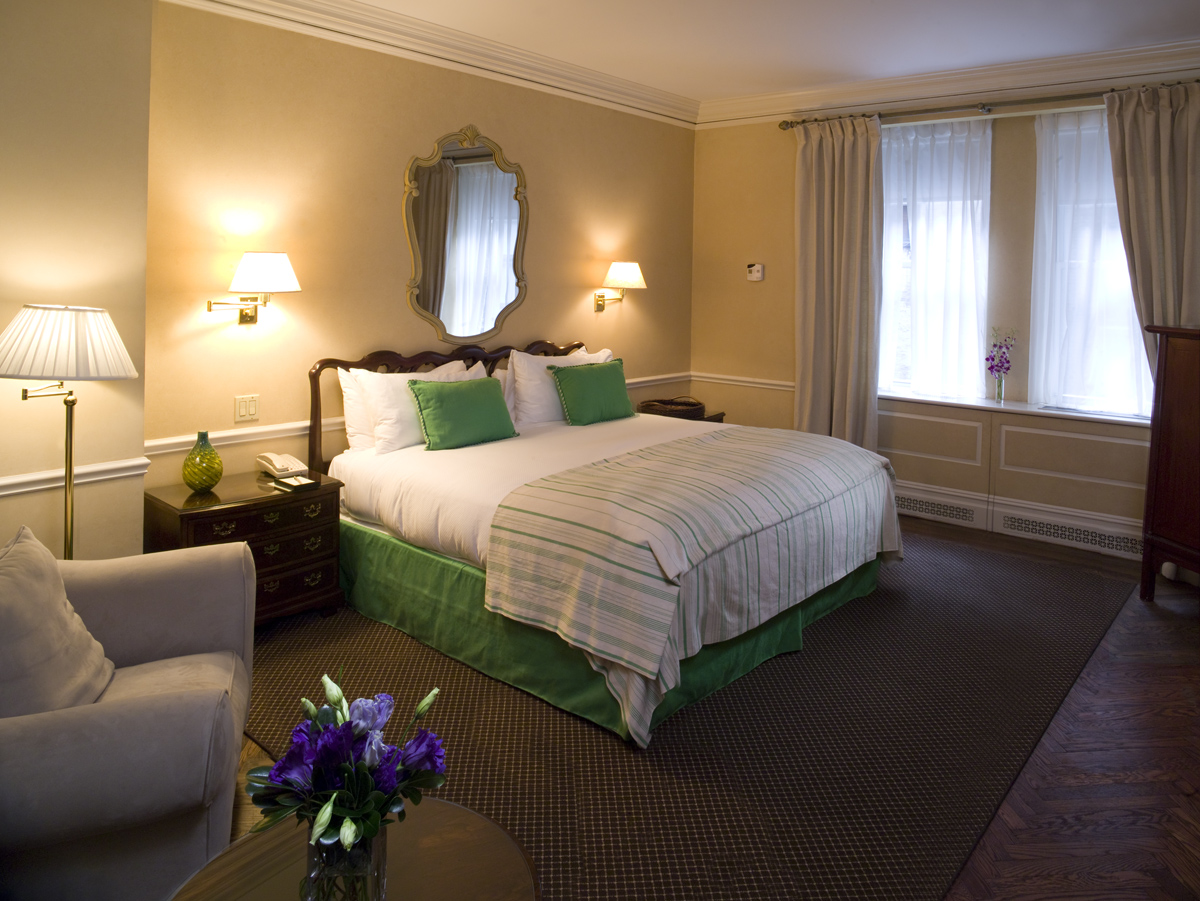 King bedroom with warm golden walls, antique wood headboard, green accent pillows, and soft lighting at the Sherry-Netherland hotel in New York City.