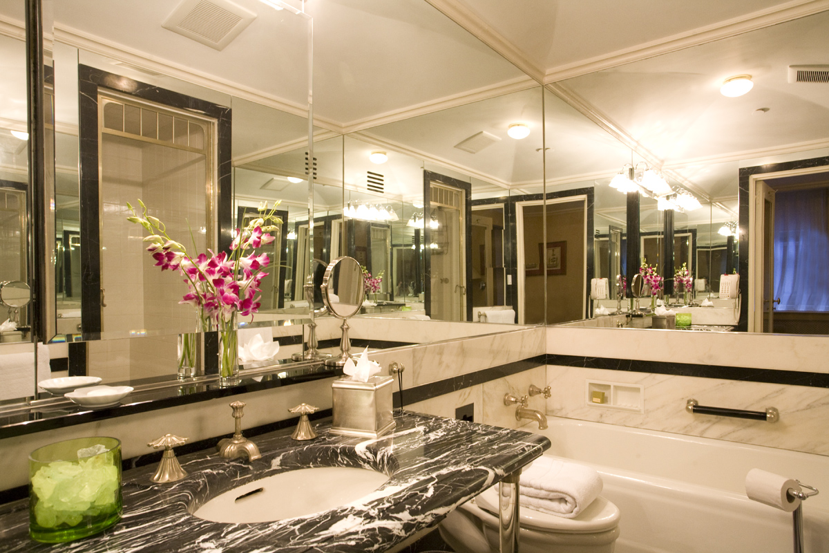 Marble bathroom with soaking tub, black and white marble vanity, mirrored walls, and fresh floral arrangement at the Sherry-Netherland hotel in New York City.