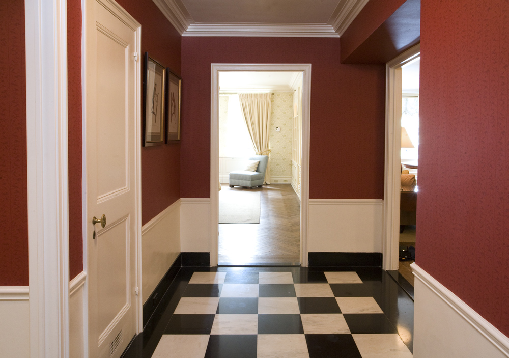 Suite entryway with black and white checkerboard marble floors, deep red walls, white crown molding, and framed artwork at the Sherry-Netherland hotel in New York City.