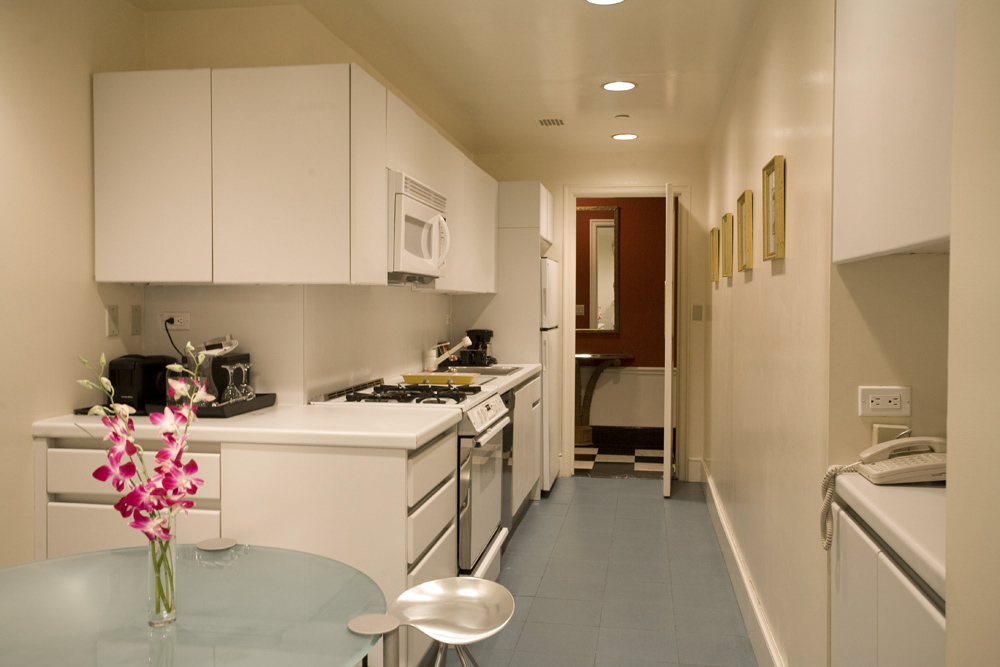 Bright, fully equipped galley kitchen with white cabinetry, gas range, coffee maker, and fresh flowers at the Sherry-Netherland hotel in New York City.