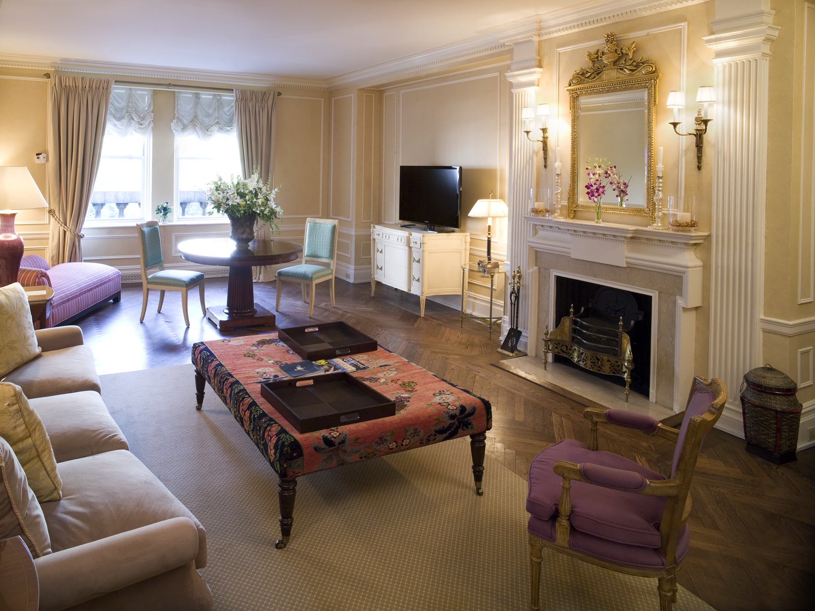 Spacious suite living room with herringbone parquet floors, ornate marble fireplace, gilded mirror, and elegant seating at the Sherry-Netherland hotel in New York City.