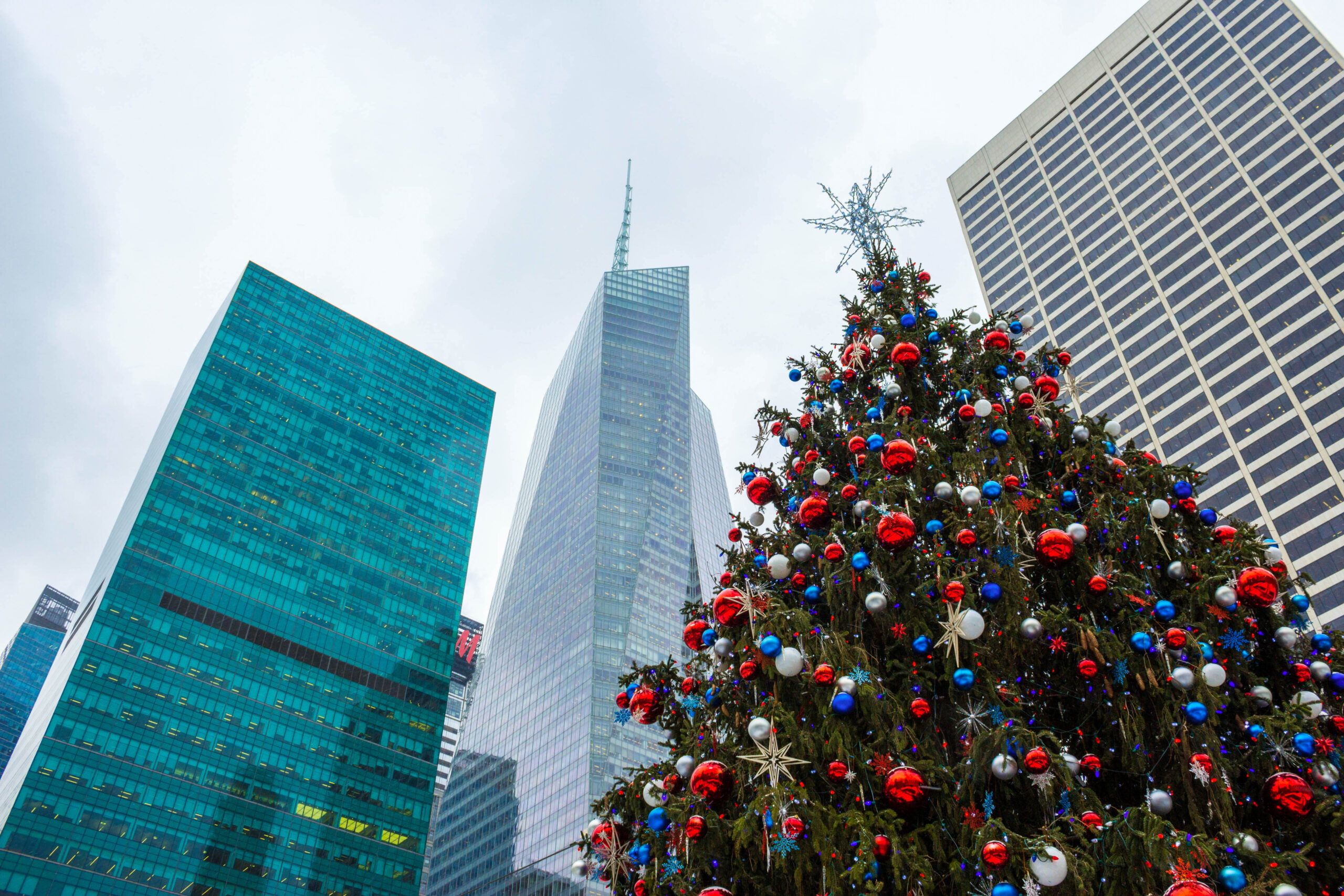 A decorated Christmas tree stands in front of tall city skyscrapers.